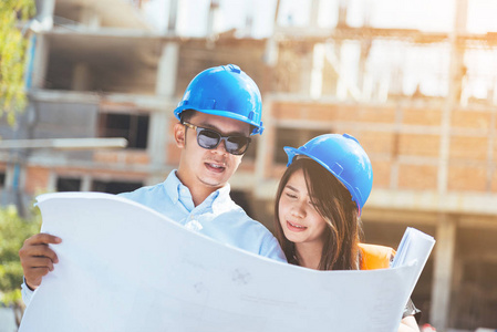 亞洲男女工程師與藍(lán)色安全頭盔會議在建筑工地與藍(lán)圖照片